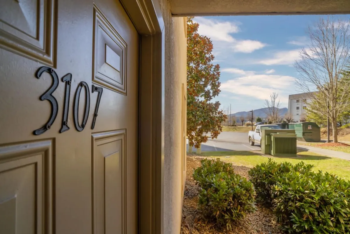 This image captures the exterior of a unit with the door number 3107, surrounded by green shrubs and set against a backdrop of street view and mountain landscape. The inviting entryway is highlighted by well-maintained greenery and distant vistas—suggesting proximity to both nature and local attractions.
