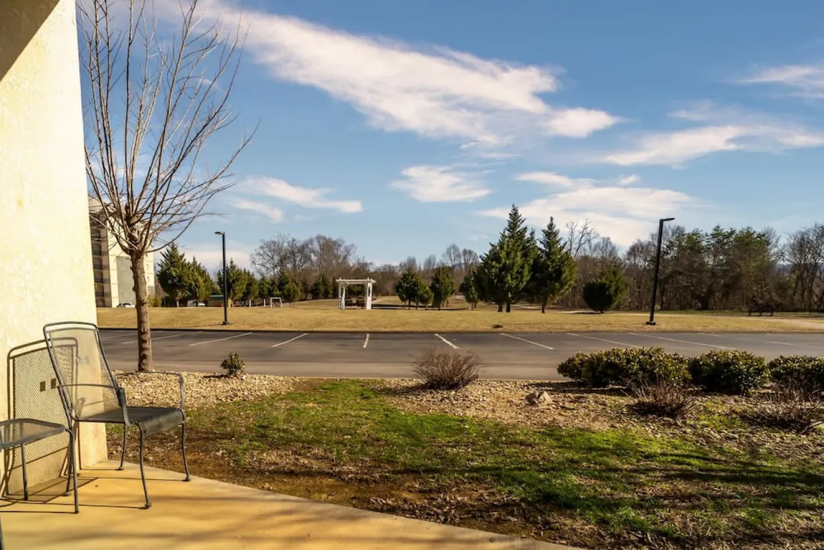 This exterior image features two metal chairs set overlooking a peaceful landscape with trees and a parking lot nearby. The setting is relaxed and welcoming, suggesting an inviting communal area where guests can enjoy the outdoors. The proximity to the parking lot also subtly hints at the convenience of complimentary parking for guests.