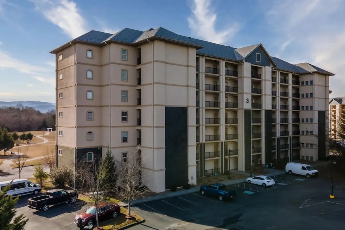 This image shows the exterior of the building, including the facade, parking area, and surrounding landscape. The view conveys ease of ground-floor access and a welcoming arrival for guests of all ages.