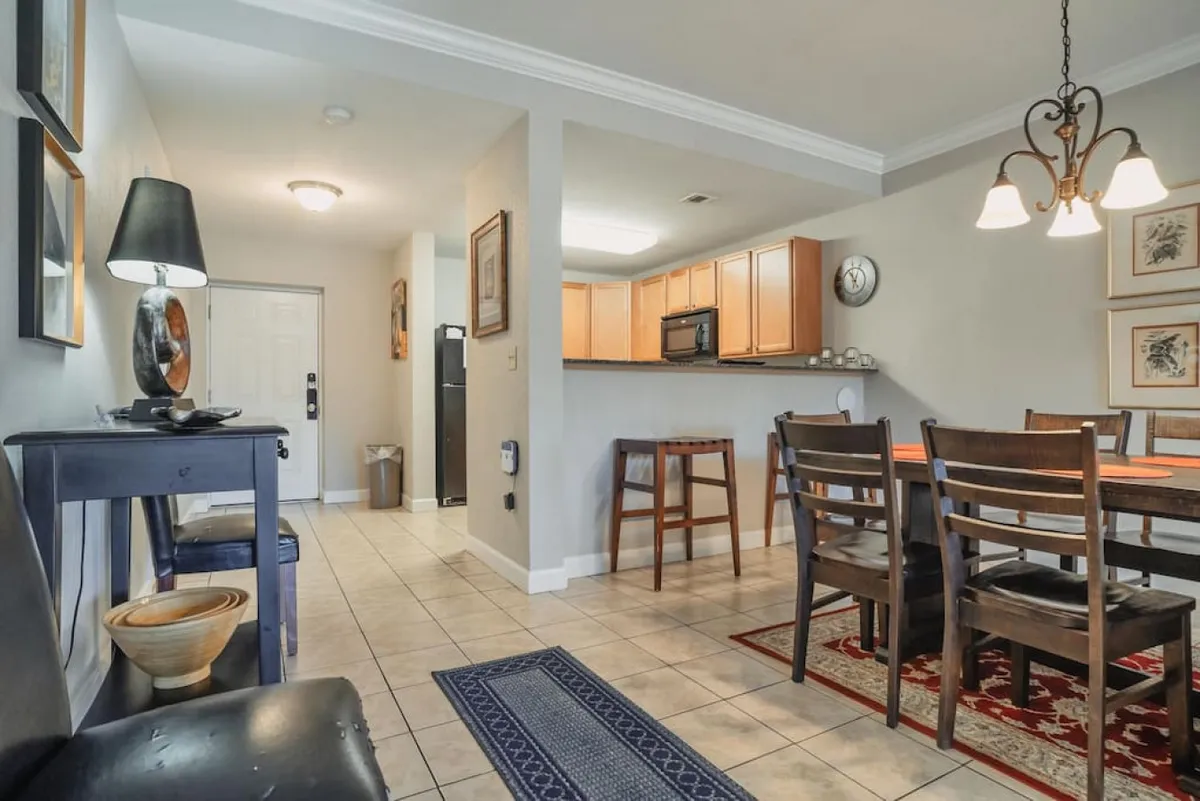 A welcoming view of the open-plan dining and kitchen area, with a spacious dining table, modern kitchen fixtures, and entryway visible. The layout emphasizes both social spaces and easy access upon arrival.