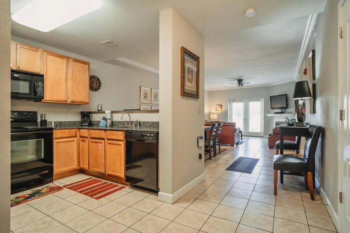 A broad interior perspective showing the kitchen area, dining table, and comfortable living room seating all in one shot. The space is filled with warm lighting, and the arrangement encourages activities like cooking, dining, and socializing.
