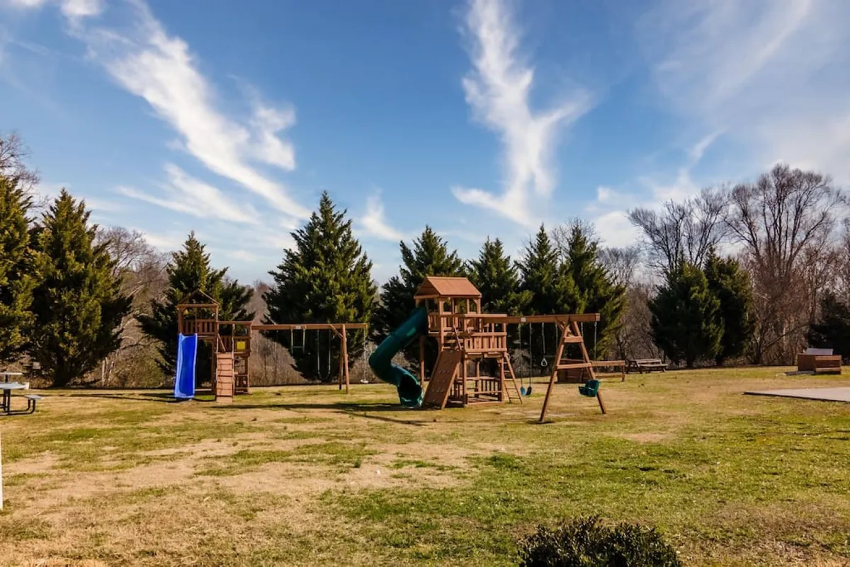 An engaging playground scene with a slide, swing set, and a nearby picnic area. Children are seen playing, with picnic tables under trees providing a perfect gathering spot for families to relax and enjoy outdoor meals while kids play safely.