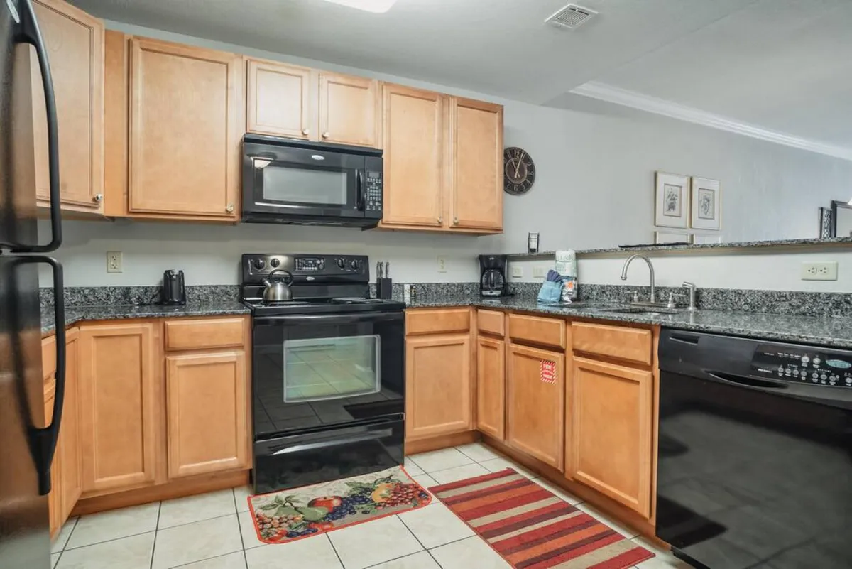 A close view of a modern kitchen with stainless steel appliances, granite countertops, rich wooden cabinetry, and a decorative rug. The kitchen is ready for meal preparation and family gatherings.